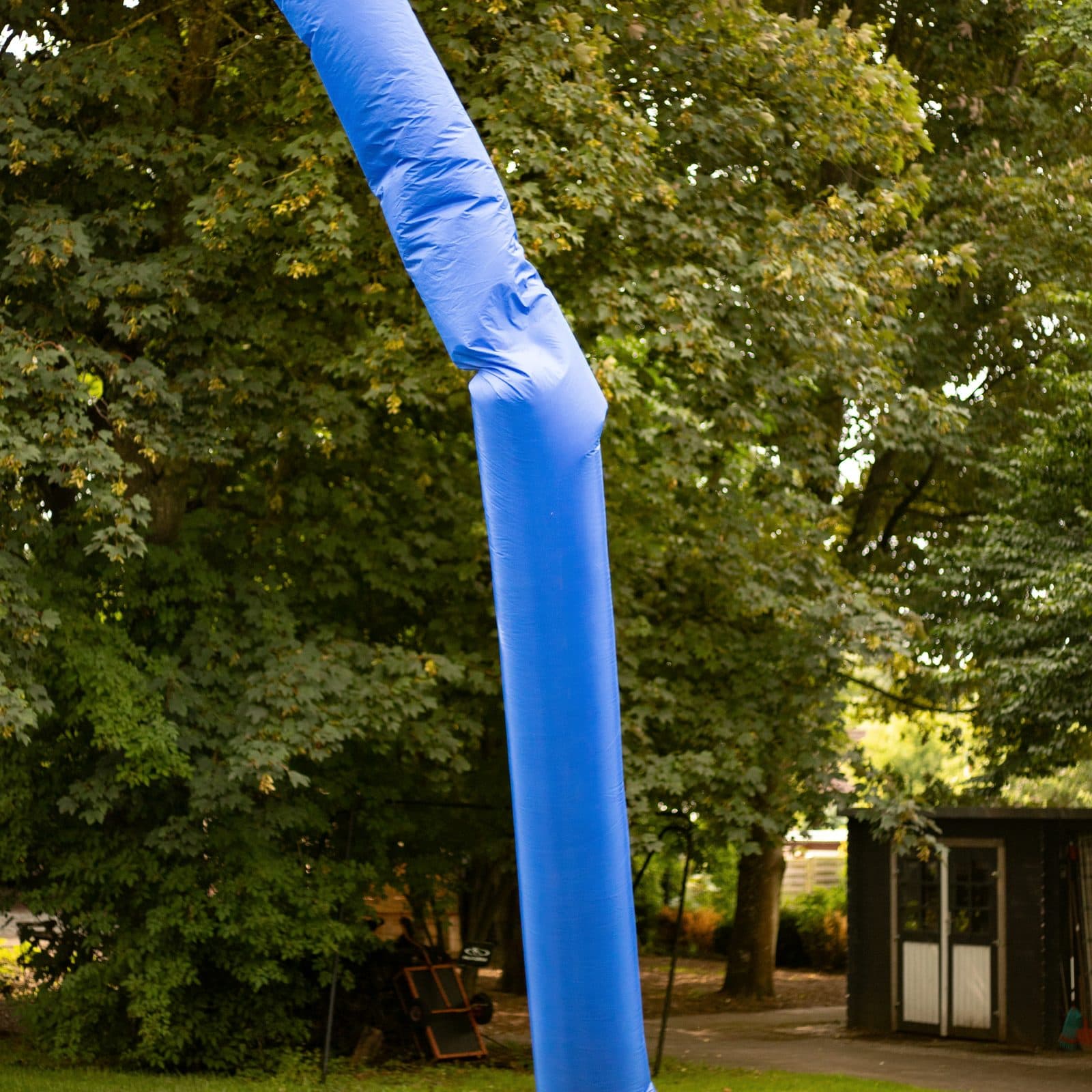 Blauer, aufblasbarer Air-Dancer winkt vor grünen Bäumen auf einer Wiese